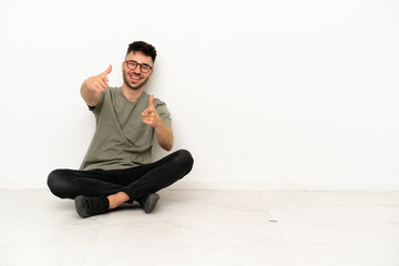 Young caucasian man sitting on the floor isolated on white background pointing to the front and smiling