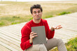 Young handsome man holding a tablet at outdoors making doubts gesture while lifting the shoulders
