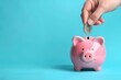 Coin is inserted by hand into a pink piggy bank on a blue background