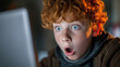 Young red-haired boy with freckles showing a look of shock and amazement at a computer screen.