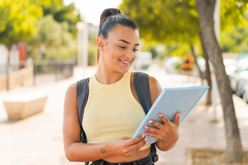 Wall Mural - Young pretty student woman at outdoors with happy expression