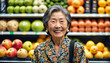 An elderly 75-year-old Asian woman smiles while shopping in the fruit section of the supermarket.