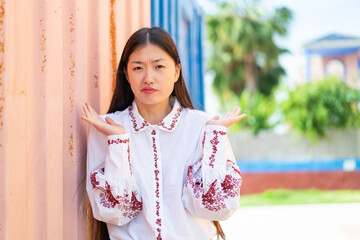 Wall Mural - Young Chinese woman at outdoors having doubts while raising hands