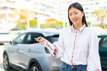 Wall Mural - Young Chinese woman at outdoors holding car keys with happy expression