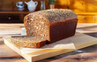 Loaf of black rye bread typical for Nordic countries and Germany. Slices on wood cutting board. Morning sunlight