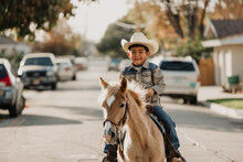 A Cheerful Young Boy Rides A Gentle Horse Down A Suburban Street, Bringing A Touch Of The Wild West To The Neighborhood