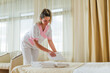 Beautiful hotel maid putting fresh and clean towels on bed in room.	