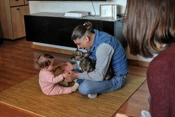 Caucasian father with his puppy fucked plays with his baby on the living room floor while mother watches in an emotional moment. Concept of family