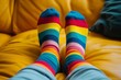 Feet clad in bright striped socks, propped up on a yellow couch, portraying leisure and vibrant fashion sense.