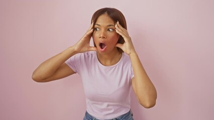 Poster - Astonishing portrait of a beautiful african american woman standing amazed and scared with wide-open mouth in disbelief, isolated over pink background