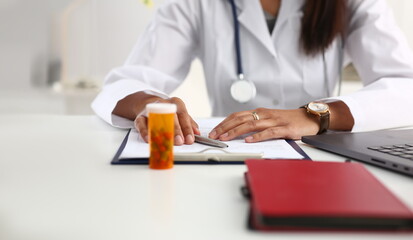 Wall Mural - Female black medicine doctor hand hold jar of pills and write prescription to patient at worktable. Panacea and life save, prescribing treatment legal drug store concept. Empty form ready to be used