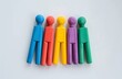 A series of wooden peg figures painted in the iconic colors of the pride flag, arranged neatly on a pristine white surface, symbolizing unity and the spectrum of LGBTQ+ identities.