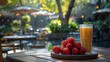 A refreshing glass of orange juice accompanied by fresh strawberries on an outdoor wooden table with a blurred garden patio background.