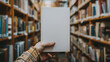 A man's hand holds a book with a blank white cover against the background of a blurred library or bookstore. Mockup, template. Day of Knowledge. World Book and Copyright Day