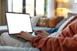 © Ihor - A person enjoying entertainment on a laptop with a white mockup screen while relaxing on a couch at home