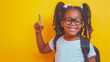 A smart young girl with glasses points upwards, wearing a white t-shirt and a backpack, against a bright yellow background. She appears ready for school, exuding confidence and cheerfulness.
