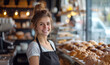 Cheerful young woman baker presents freshly baked pastries in coffee shop with warm smile and golden flaky treats create inviting atmosphere with blurred background activity, add to charm of scene