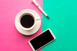 Flat lay photo with coffee cup, mobile phone and pen on geometric green and pink background. Top view, minimal concept