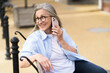 A woman is sitting on a bench and talking on her cell phone. She is smiling and she is enjoying her conversation