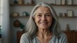 © Muqaddas - Happy confident senior woman with long naturally grey hair standing in home interior, looking at camera with crossed arms, smiling, posing for head shot vertical front portrait