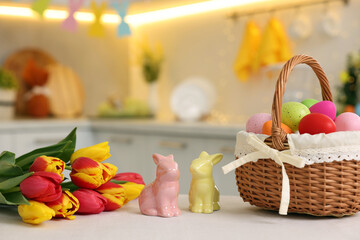 Sticker - Easter decorations. Wicker basket with painted eggs, tulips and bunny figures on white table indoors, closeup