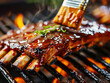 Glazed barbecue ribs on a grill with a basting brush and vibrant flames