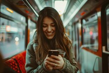 A Young Woman With A Radiant Smile Looks Down At Her Phone While Riding On A Subway Train