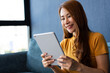© Prot - Portrait of Young attractive asian woman resting on sofa and using and looking at tablet pc in modern room communication and lifestyle concept. reading digital gadget at house.