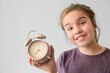 A girl is holding a pink alarm clock with the time of early morning