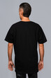 Man dressed in a black oversized t-shirt with blank space, ideal for a mockup, set against gray background