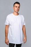 Fototapeta  - Man dressed in a white oversized t-shirt with blank space, ideal for a mockup, set against gray background