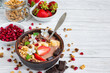 Chocolate smoothie bowl topped with oat granola, banana, strawberries, pomegranate and spring flowers on white wooden table. Healthy vegan protein food with cocoa for breakfast