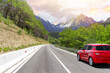 A red car drives along the highway against the backdrop of rocky mountains and tunnel on a sunny day.