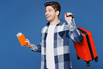 Poster - Traveler man wears shirt casual clothes hold bag passport ticket look aside isolated on plain blue background. Tourist travel abroad in free spare time rest getaway. Air flight trip journey concept.