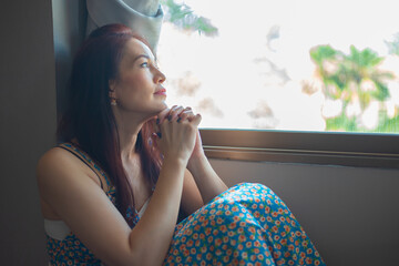 Wall Mural - Asian woman praying near the window in room, Hands folded in prayer concept for faith,spirituality and religion.