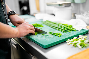 Wall Mural - A skilled chef meticulously chops fresh green onions on a cutting board in a professional kitchen. The vibrant green hues and precise movements evoke culinary artistry