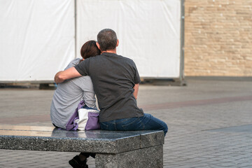 In the serene romantic embrace of a man and a woman, two souls are comforted on an outdoor city bench, their tender connection speaks of the importance of understanding and intimacy