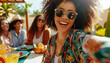 A radiant woman with curly hair takes a selfie with friends at a sunny outdoor gathering, her joy infectious.