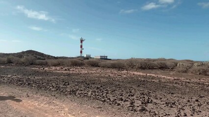 Wall Mural - Active senior man with cap and walking sticks enjoys freedom and healthy lifestyle on sunny day hiking outdoors, nature reserve in southern Tenerife, lighthouse in background