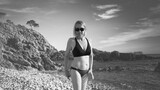 Fototapeta  - woman with black sunglasses and hat walking on the sandy beach. black and white image