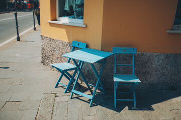 A terrace with a small blue table and chairs. cosy street with colorful chairs in italian city.