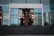 © qunica.com - Group of businesspeople exiting a building, engaged in conversation about a new project and strategizing for profitability.