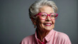 Strahlendes Lächeln einer Seniorin mit pinker Brille vor grauem Hintergrund
