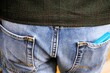 Rückenansicht von jungem Mann mit blauer Jeanshose und grauer Weste aus Wolle mit blauem Handy in Hosentasche 