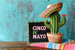 Concepto de celebracion del 5 de mayo en Mexico. Maceta con cactus con sombrero charro sobre tabla de madera ,  fondo grunge turquesa y cartel