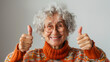 Femme joyeuse levant les pouces en l'air, photographie sur fond blanc, grand-mère de 70 ans avec des lunettes et un col roulé