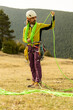 © VICTOR - A man in a yellow jacket and green scarf is holding a green rope. He is standing in a field with a mountain in the background