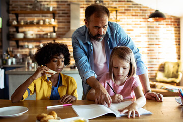 father helping children with homework at kitchen table