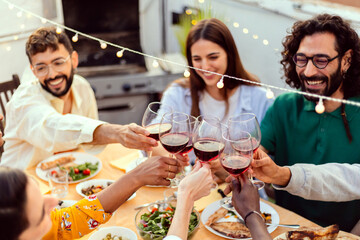 Wall Mural - Group of young friends drinking red wine enjoying summer barbecue at rooftop terrace. Diverse people having fun at dinner party