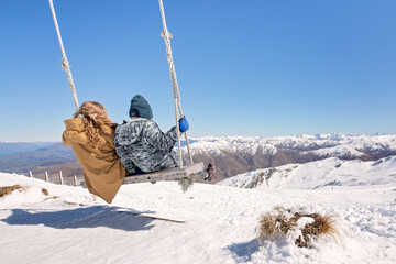 two children swing away above snow covered alpine mountain vista Cardrona New Zealand